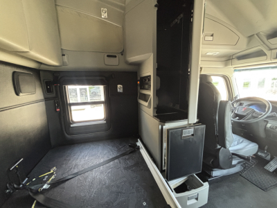 Kenworth T680 cab interior showing sleeper area and driver seat with dashboard; visible storage cabinets and window.