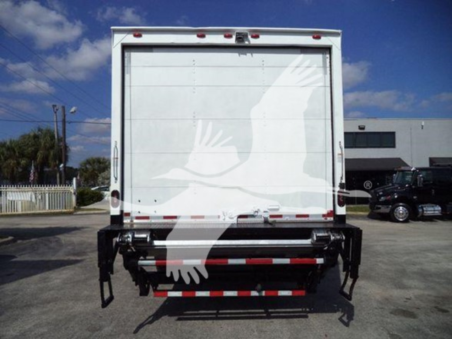 Back of a 2018 Isuzu FTR box truck with a white tailgate and a rear bumper/step, showing a crane-like platform and a white graphic on the door.
