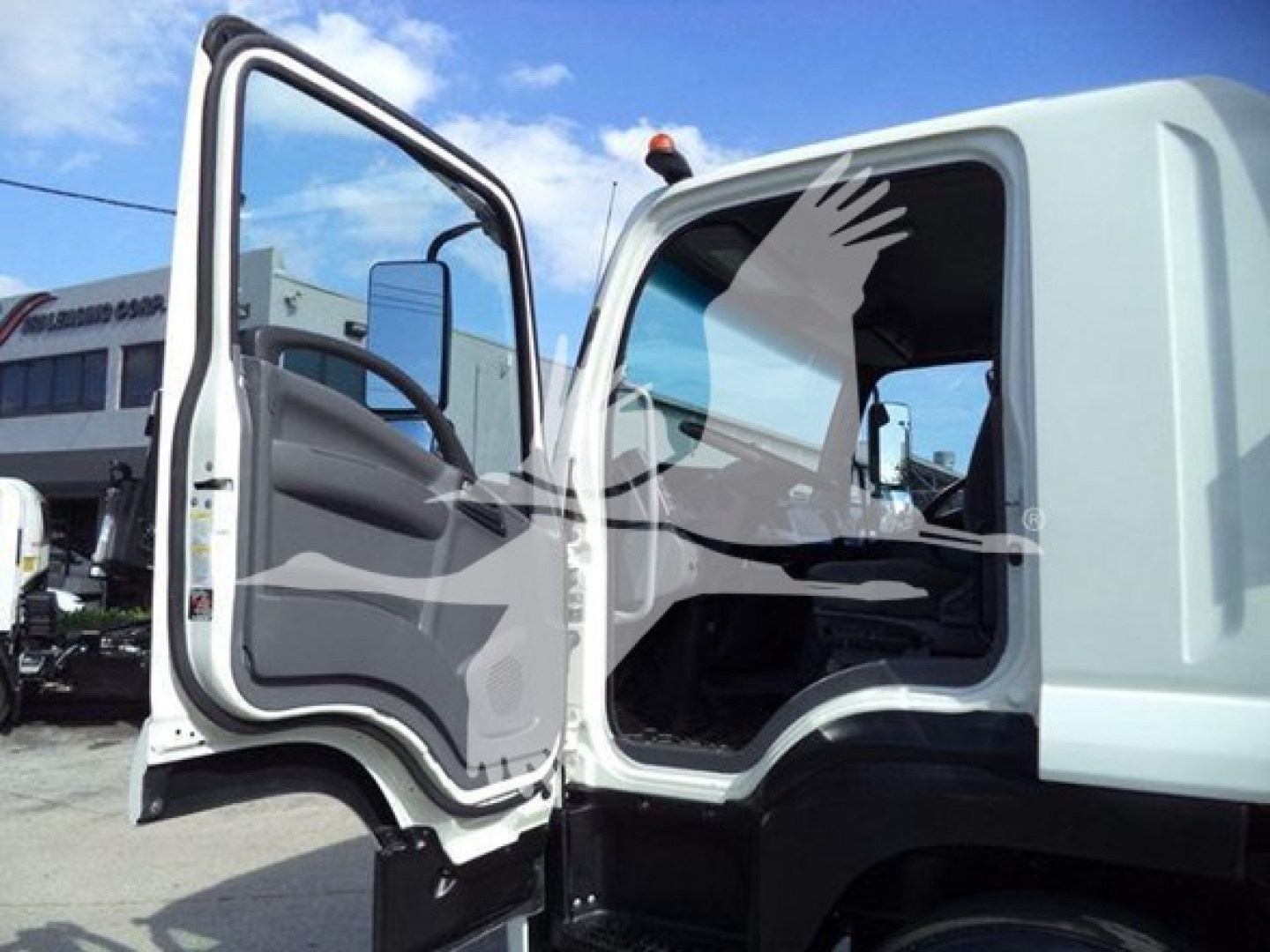 Isuzu FTR truck cab with door open, showing interior steering wheel and dashboard, white exterior, blue sky.