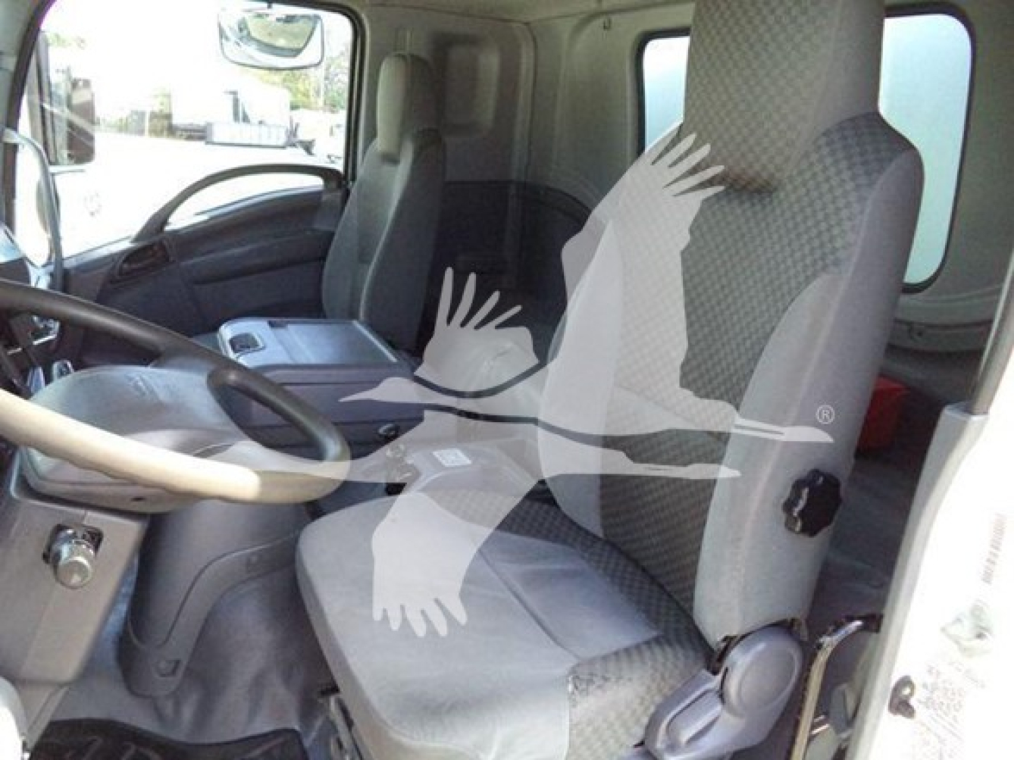 Isuzu FTR interior cabin view showing driver seat and passenger seat in front cab. Visible dashboard steering wheel and center console.