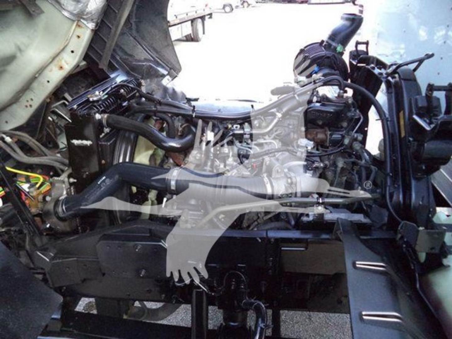 Isuzu FTR engine bay showing front-mounted diesel engine and hoses in a box truck, with visible intake and coolant lines.