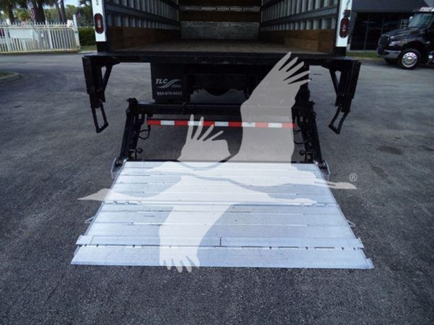 Isuzu FTR rear view with hydraulic lift and lowered aluminum ramp. Medical overlay of hands and logo superimposed