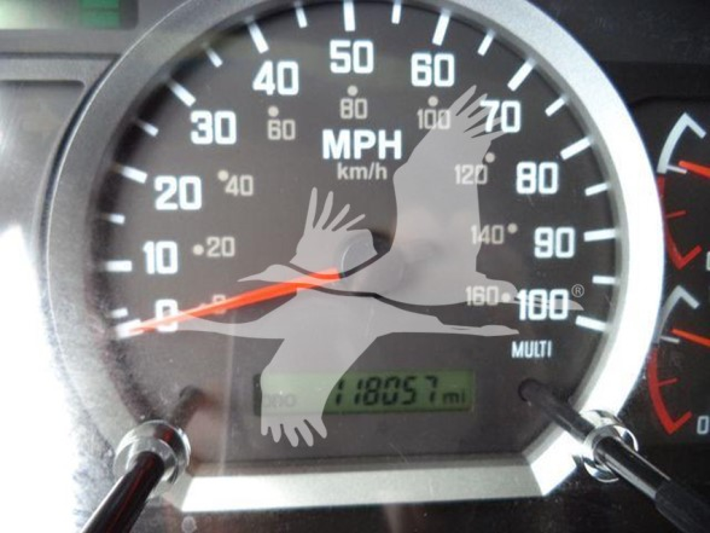 Speedometer gauge showing mph and km/h with odometer reading 18057 miles. Dashboard with black dial, white numbers, orange needle.