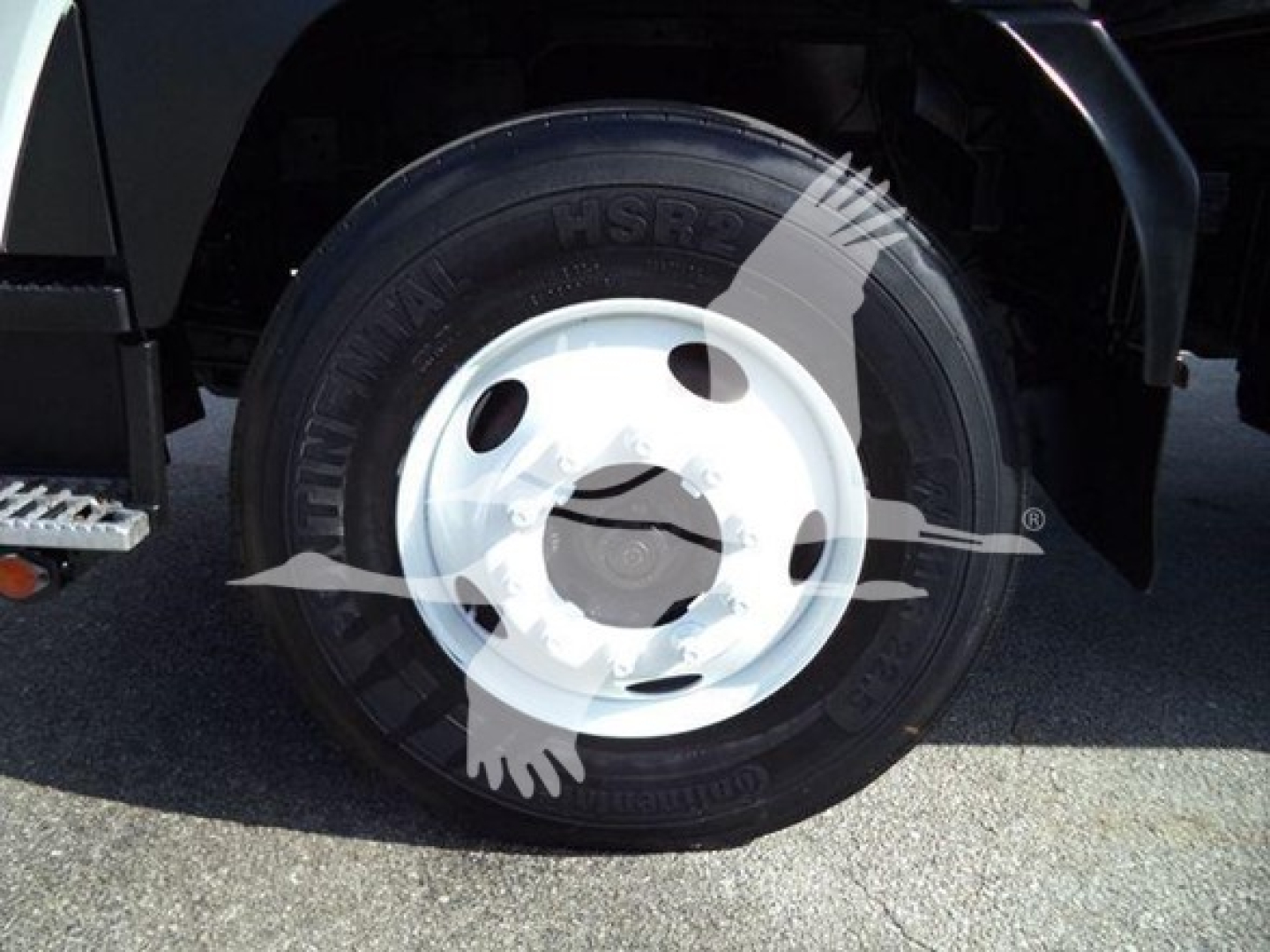 Isuzu truck wheel and tire in near-side front, with white wheel rim and black tire. Text on tire reads ‘Continental HSR’ and other tire markings faintly visible.