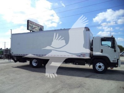 Isuzu box truck side view showing cargo box and cab; visible text on sign in background: TLC Truck Sales & Service.