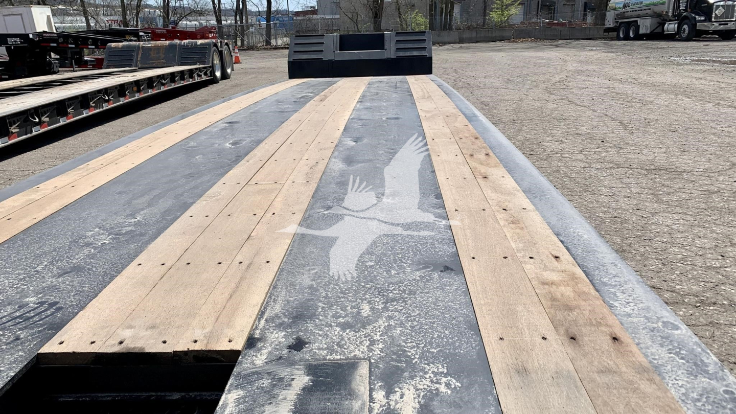 Flatbed trailer deck with wooden planks and metal framework, Fontaine Renegade N12 appearance, view from front toward cab area, light-gray weathered surface