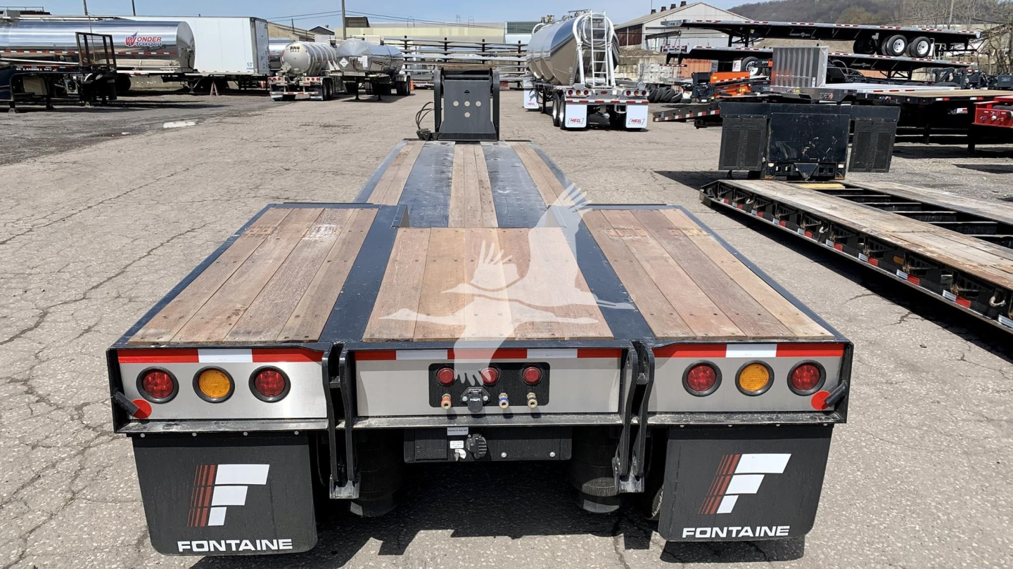 Fontaine Renegade N12 lowboy trailer rear view showing tail lights, mud flaps with Fontaine logo, wooden bed with metal striping, and hitch area.