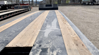 Flatbed trailer deck with wooden planks and metal framework, Fontaine Renegade N12 appearance, view from front toward cab area, light-gray weathered surface
