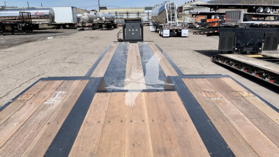 Fourteen-foot trailer deck with wood planks and black steel bands. In background are other trailers, tanks, and equipment on a lot.