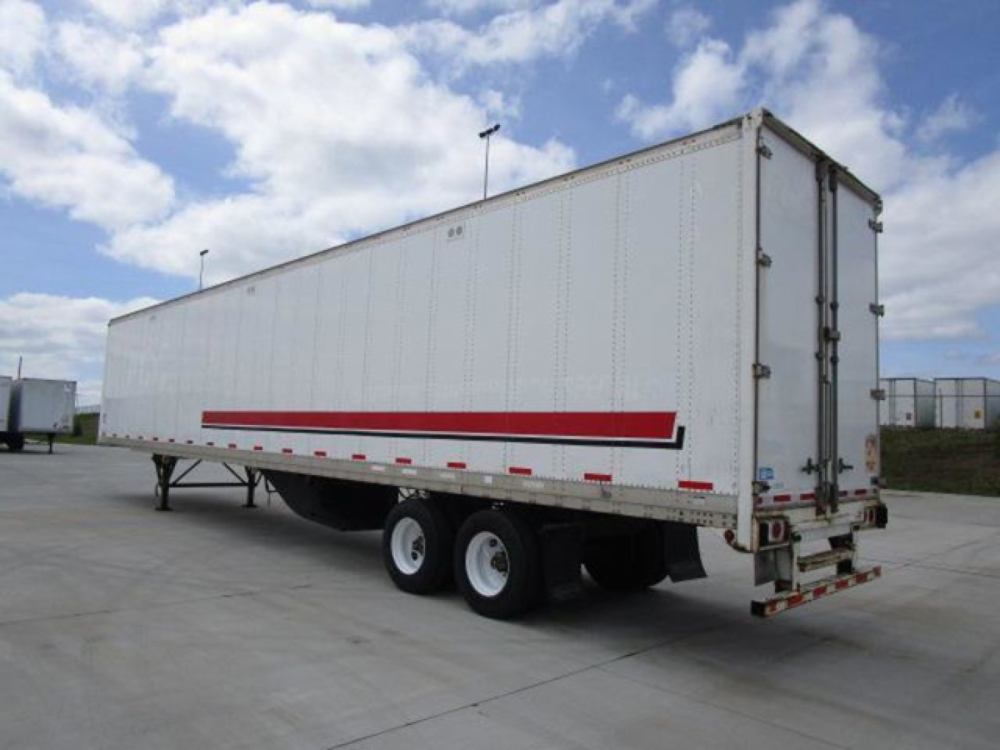 Trailer side and rear view showing a white Stoughton van trailer with a red stripe, dual rear axles, and rear doors.