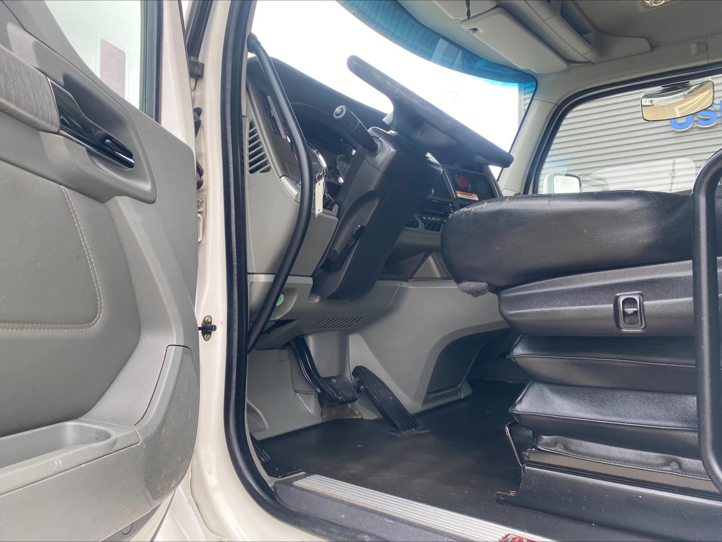 Interior of a 2018 Kenworth T880 cab showing driver’s seat, steering wheel, and dashboard with entry door open.