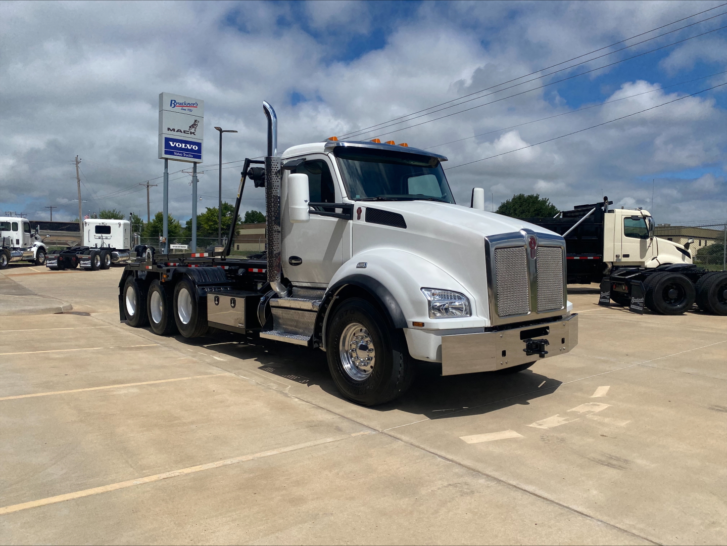 Kenworth T880 roll-off truck in white, front three-quarter view, with chrome bumper and dual exhaust stacks visible.