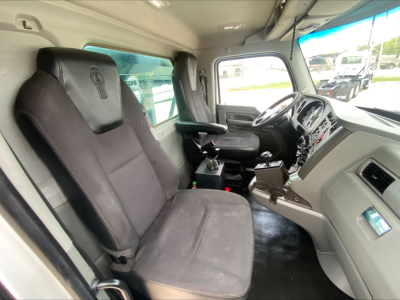 Kenworth T880 cab interior showing driver and passenger seats, steering wheel, dashboard, and center console from the entry door, with light gray panels.