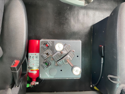 Kenworth T880 wheelbase cab interior showing control panel with switches, two gauges, red fire extinguisher, and seat backs.
