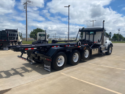 Kenworth T880 roll-off truck in serviceable condition showing flatbed/loader with multiple axles and rear towing hitch. Cab with sleeper, black chassis, and raised exhaust.