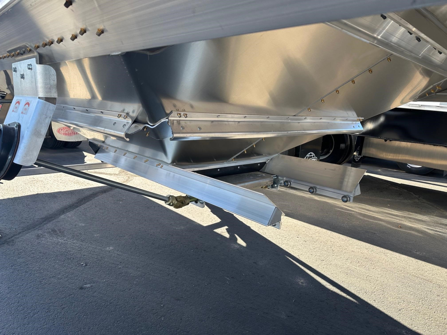 Trailer undercarriage with metal hopper and support beams, hitch and landing gear visible.