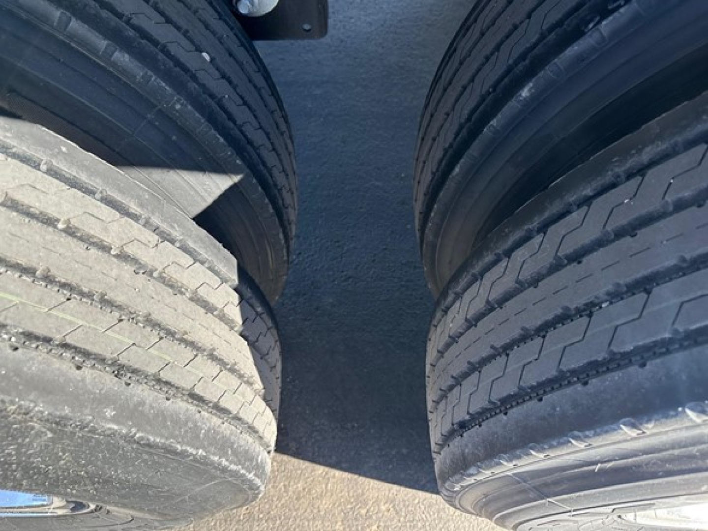 Two rear wheels and a gap between them on a trailer, showing tire treads and a dark road surface between.