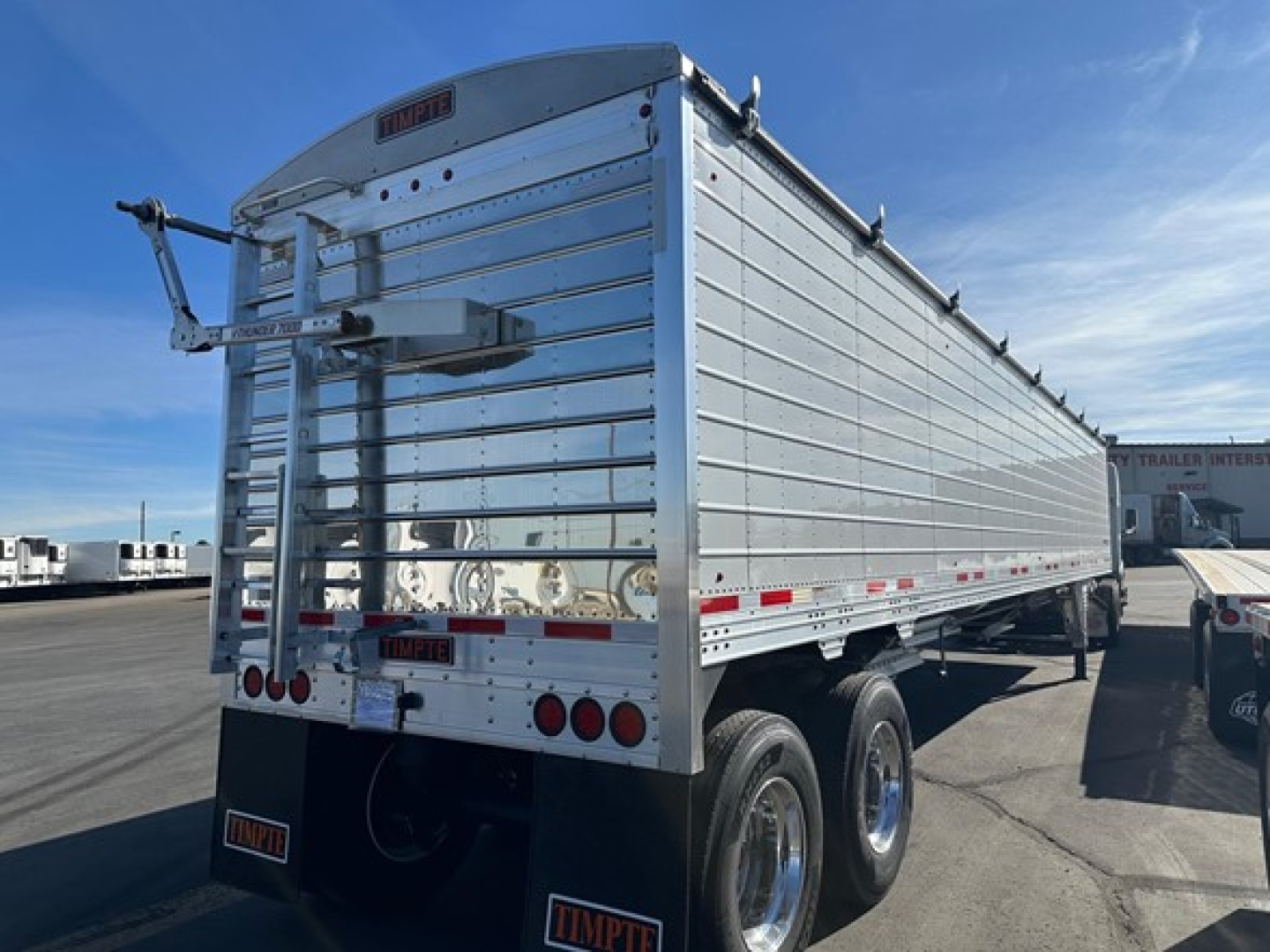 Timpte Super Hopper W trailer rear and side view showing aluminum panels, dual axle wheels, and rear gate with latches and emergency brake lever.