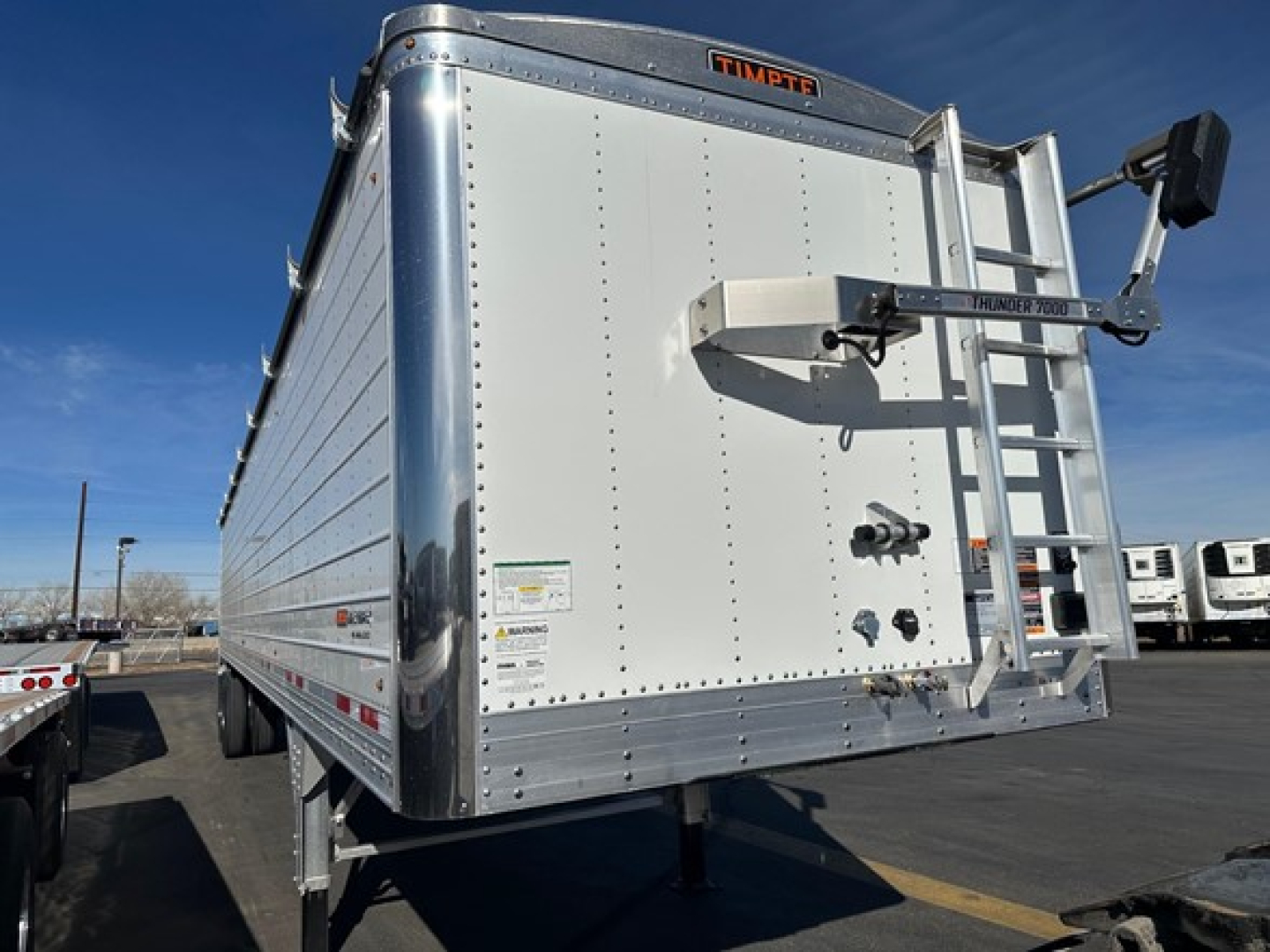 Trailer rear view showing Timpte Super Hopper W with ladder, hinged rear door, reflective tape, and safety decals.