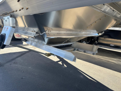 Trailer undercarriage with metal hopper and support beams, hitch and landing gear visible.