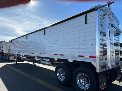 Trailer side view showing white Timpte Super Hopper W trailer with dual rear wheels, ladder at back, and reflective strips.
