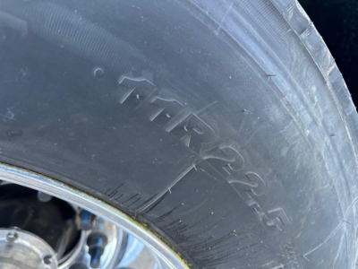 Tire sidewall showing TIMR? 22.5 or similar model code on a trailer wheel, detail of tire with worn tread and lettering.
