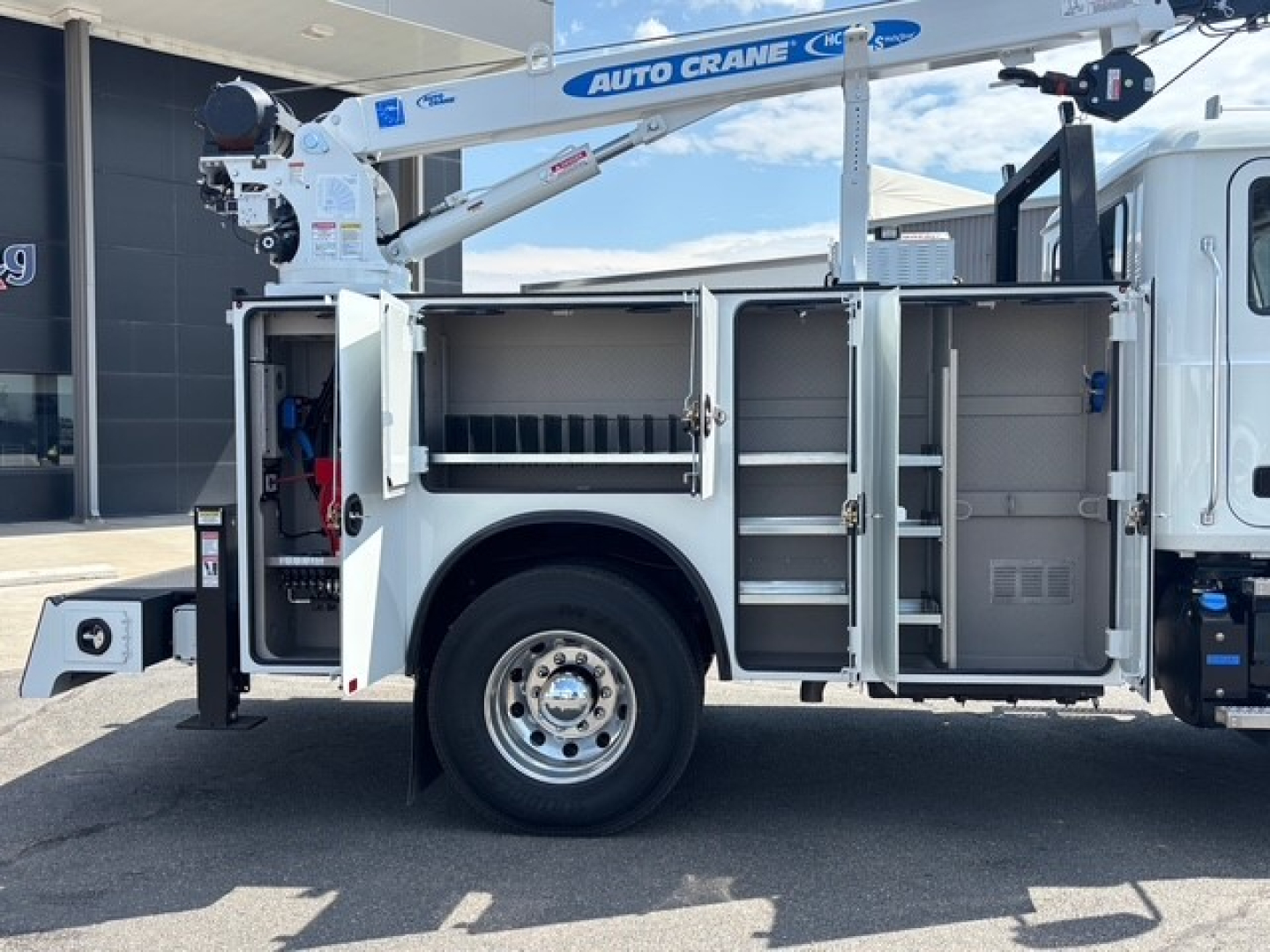Service/utility truck side compartments opened revealing storage racks and equipment, built on a 2026 Mack MD6 with a crane mounted above.