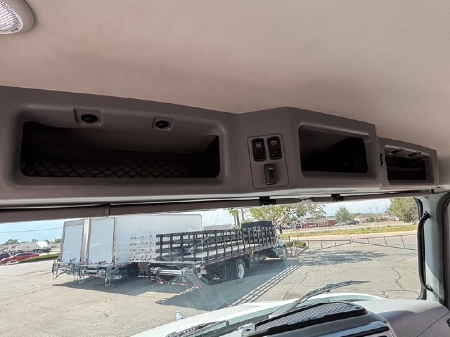 Mack MD6 cab interior overhead storage and controls visible from windshield, with exterior yard in background.