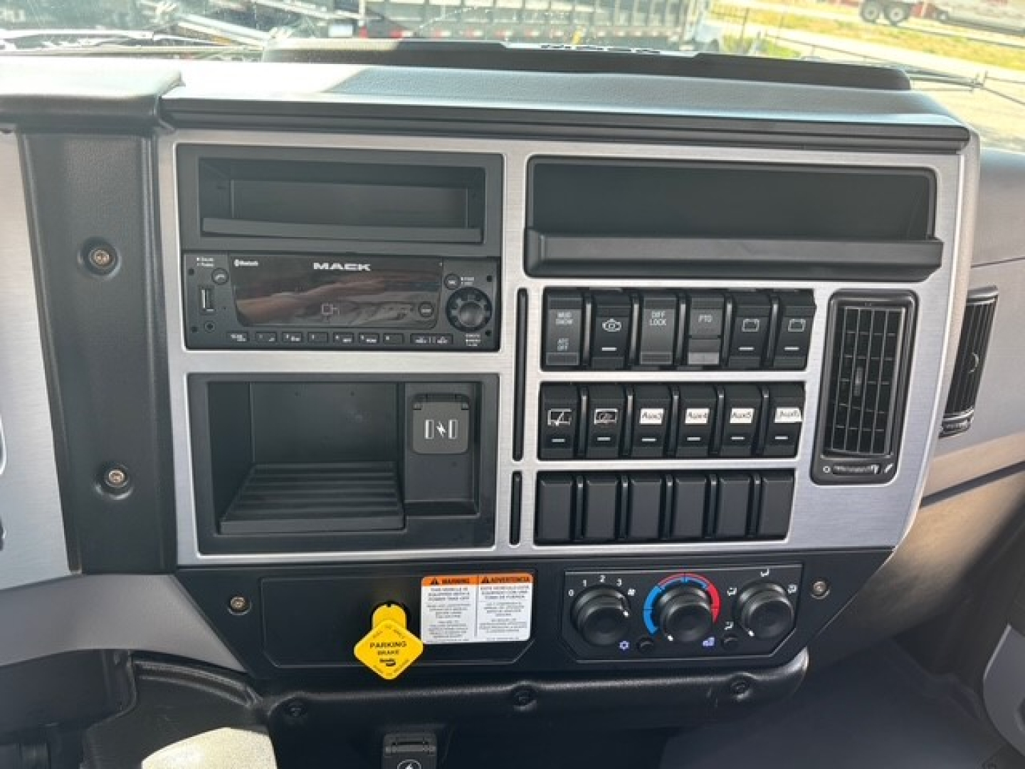 Dashboard of a 2026 Mack MD6 showing radio, controls, and climate knobs; center console with switches and a yellow key tag visible.