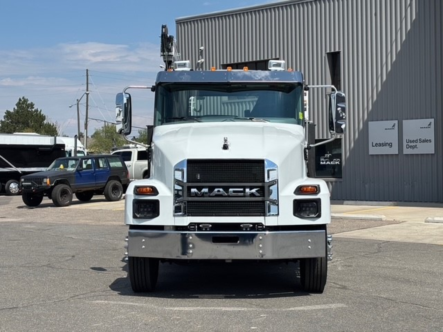 Front view of a white 2026 Mack MD6 service/utility truck showing large chrome grille with MAC K letters, bumper, headlights, and side mirrors.