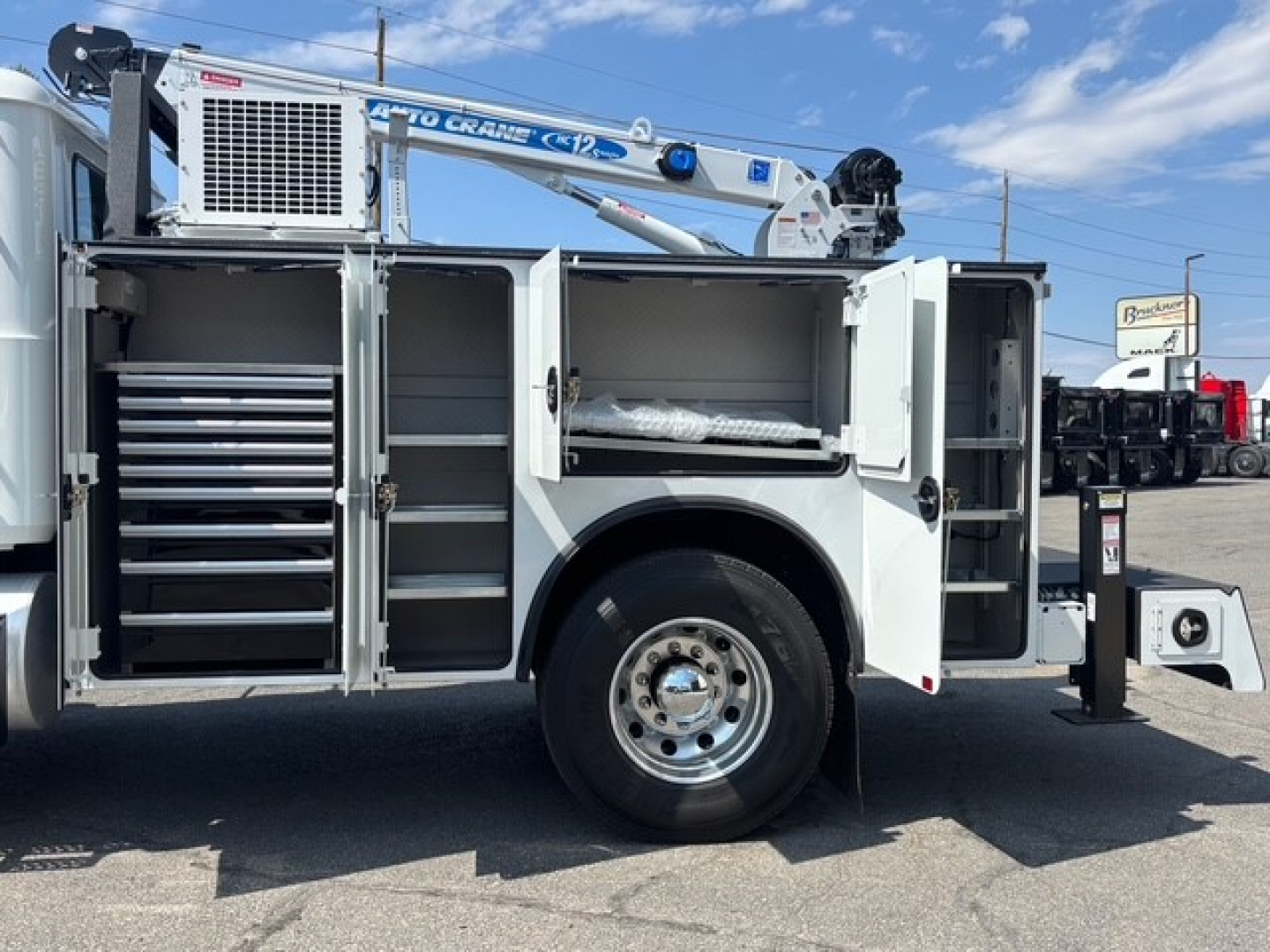 Mack MD6 service truck with open side compartments and hydraulic lift, showing tool drawers and storage boxes on both sides.