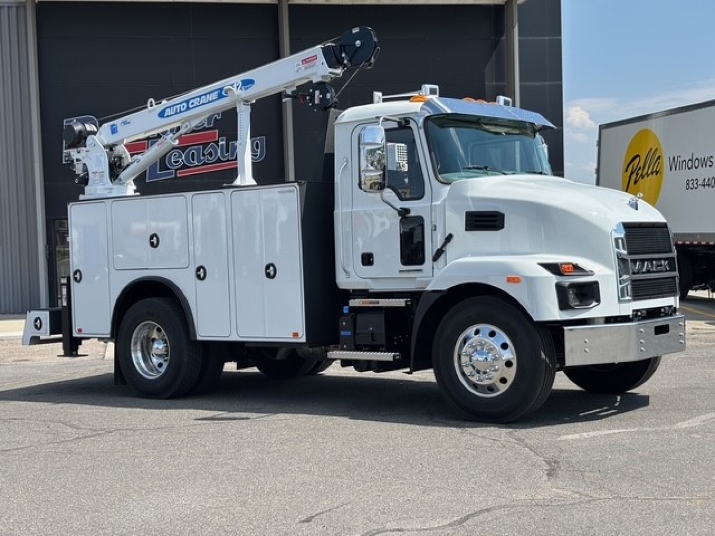 Mack MD6 service truck with crane boom and utility compartments, white cab, crane mounted over bed, side compartments visible.