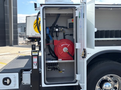 Service/utility truck utility cabinet inside open compartment showing coiled red hose reel, hoses and fittings, electrical panel, and wiring harnesses.