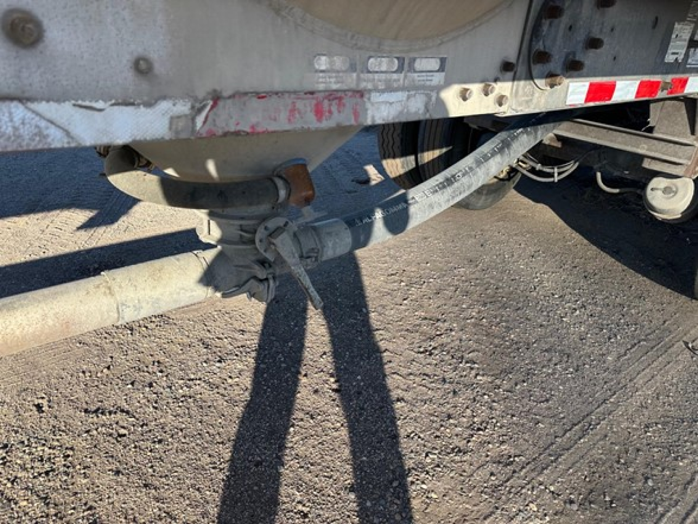 Pneumatic trailer hitch and undercarriage showing coupling and piping with metal frame and dirt road surface.