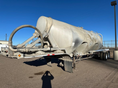 Pneumatic dry bulk trailer in service with cylindrical tank, rear chute and hoses visible. Side view shows tandem axles and support braces.
