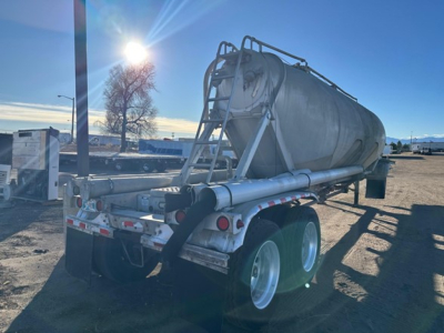 Pneumatic dry bulk trailer in-use showing rear and right side with dual axles and cylindrical tank.