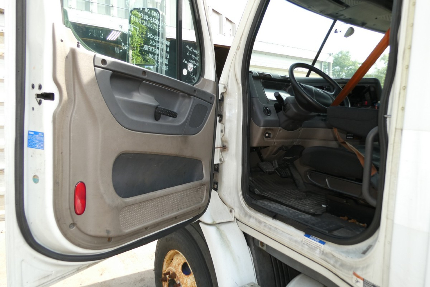 Freightliner Cascadia 113 cab interior and open door view in a truck yard showing steering wheel and driver seat.