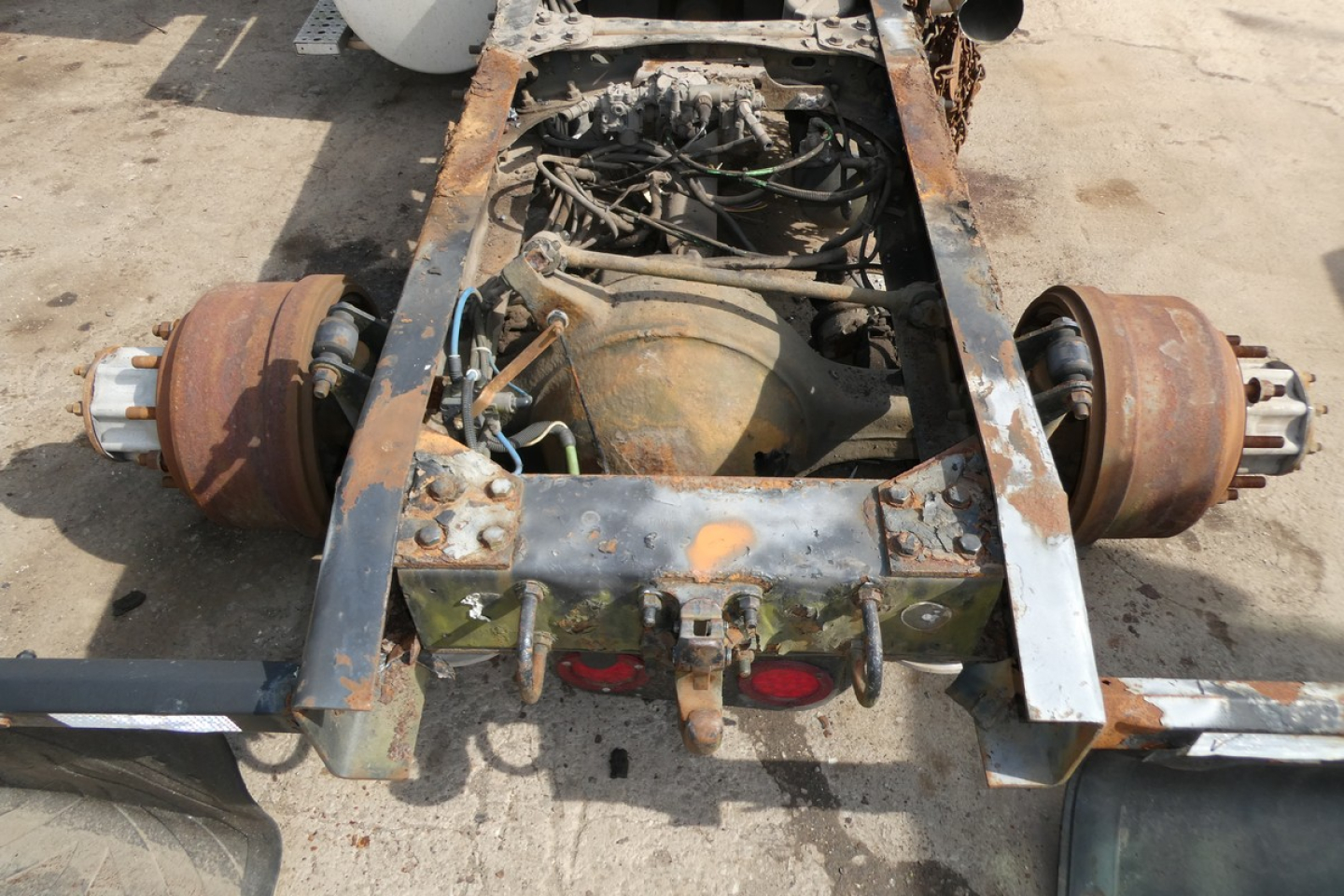 Drivetrain area of a Freightliner Cascadia 113 chassis showing rusted rear axles and exposed engine from a toppled view.