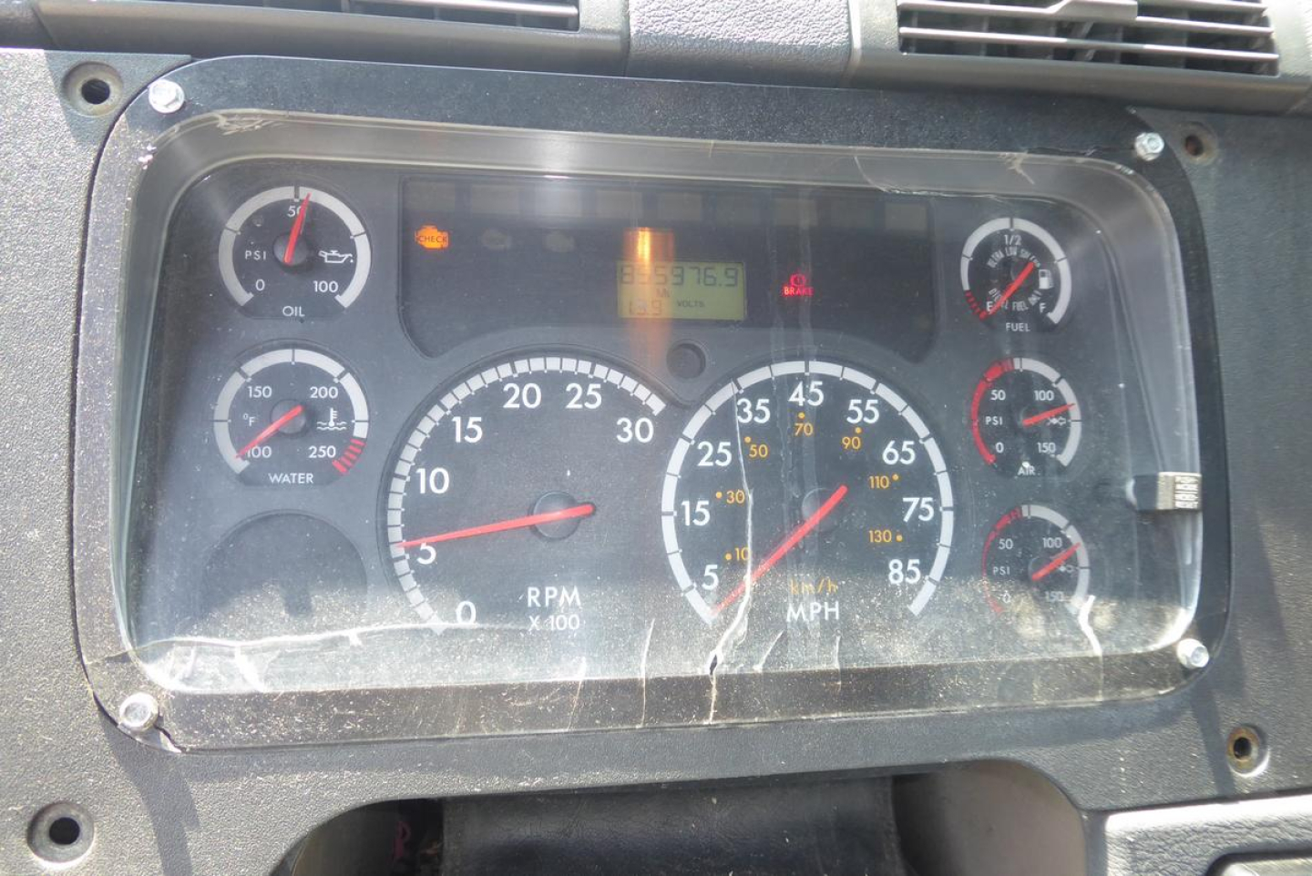 Dashboard cluster of a Freightliner Cascadia 113 showing gauges (RPM, speedometer, fuel, oil, water) and warning lights behind a glass cover.