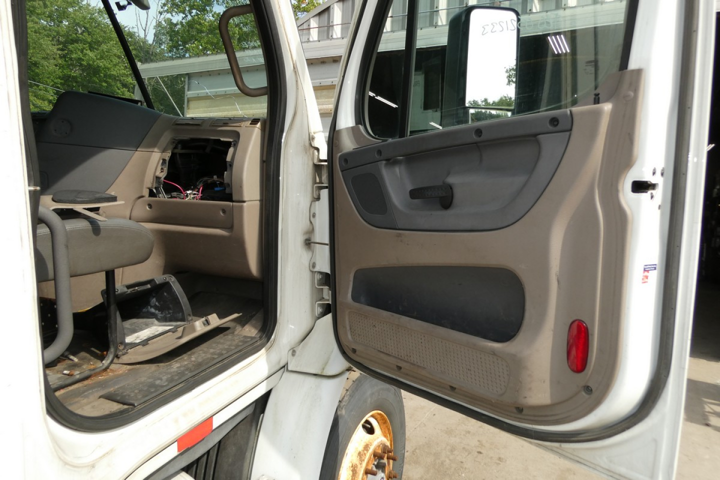 Cab interior of a Freightliner Cascadia 113 daycab showing open driver and passenger doors with beige panels and exposed wiring.