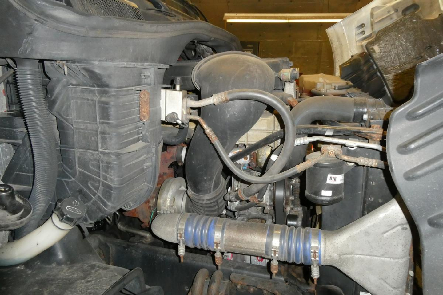 Freightliner Cascadia 113 engine bay showing air intake and hoses, black plastic reservoir, blue hose clamps, and surrounding components.