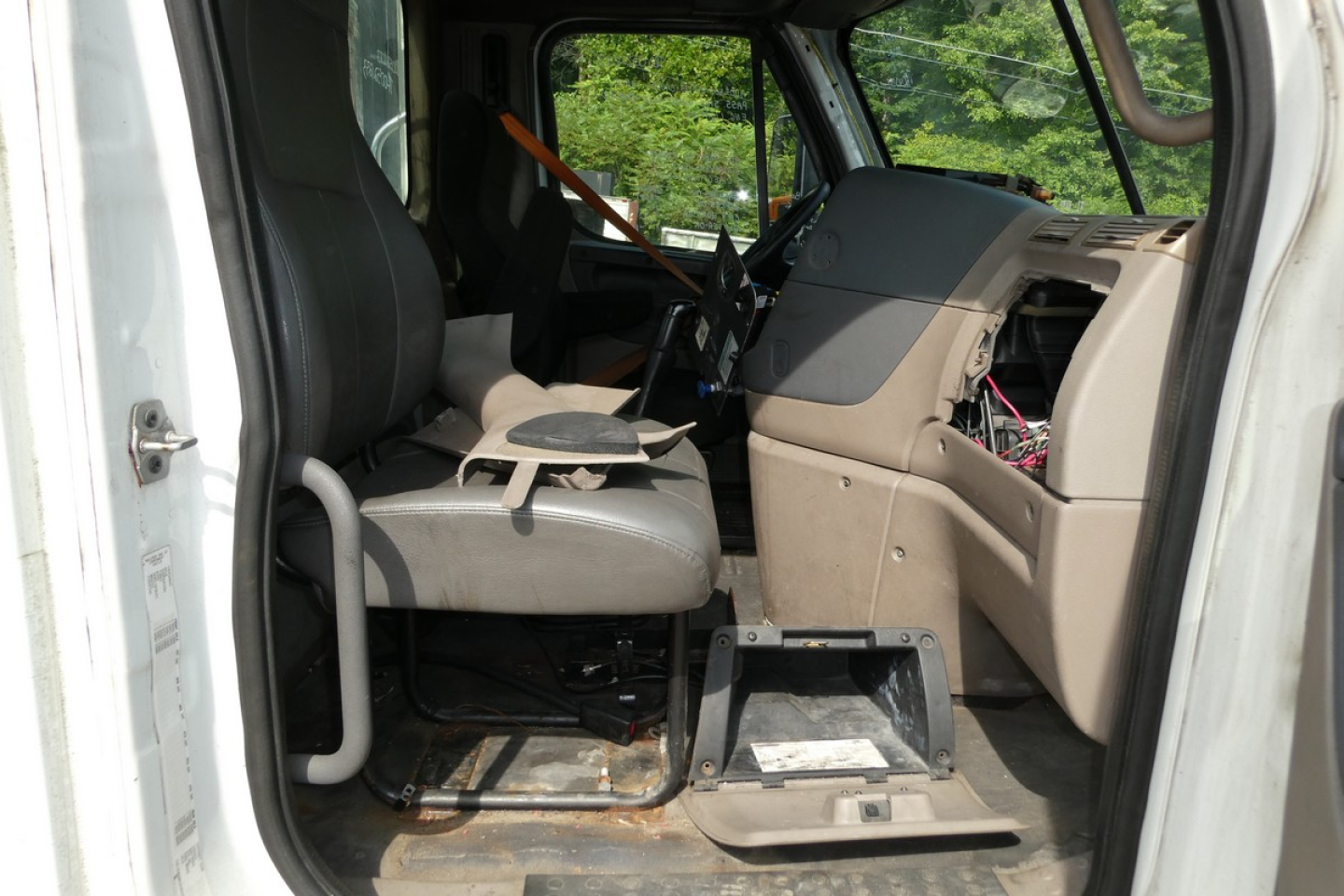 Cab interior of a Freightliner Cascadia daycab showing driver seat, dashboard, and steering column.