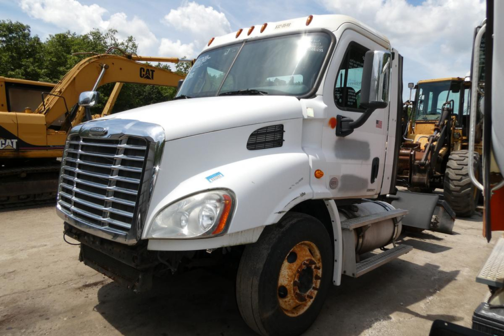 Truck cab front view of a white Freightliner Cascadia 113 conventional daycab with chrome grille, black mirrors, and yellow wheels in a yard.