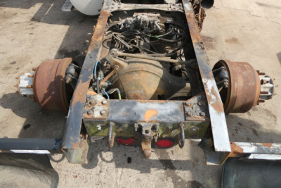 Drivetrain area of a Freightliner Cascadia 113 chassis showing rusted rear axles and exposed engine from a toppled view.