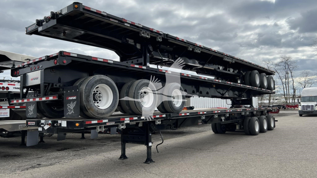 Manac extendable flatbed trailer viewed from side with dual rear axles and extendable deck; visible labels include Manac branding and chain binders; trailer parked on lot.