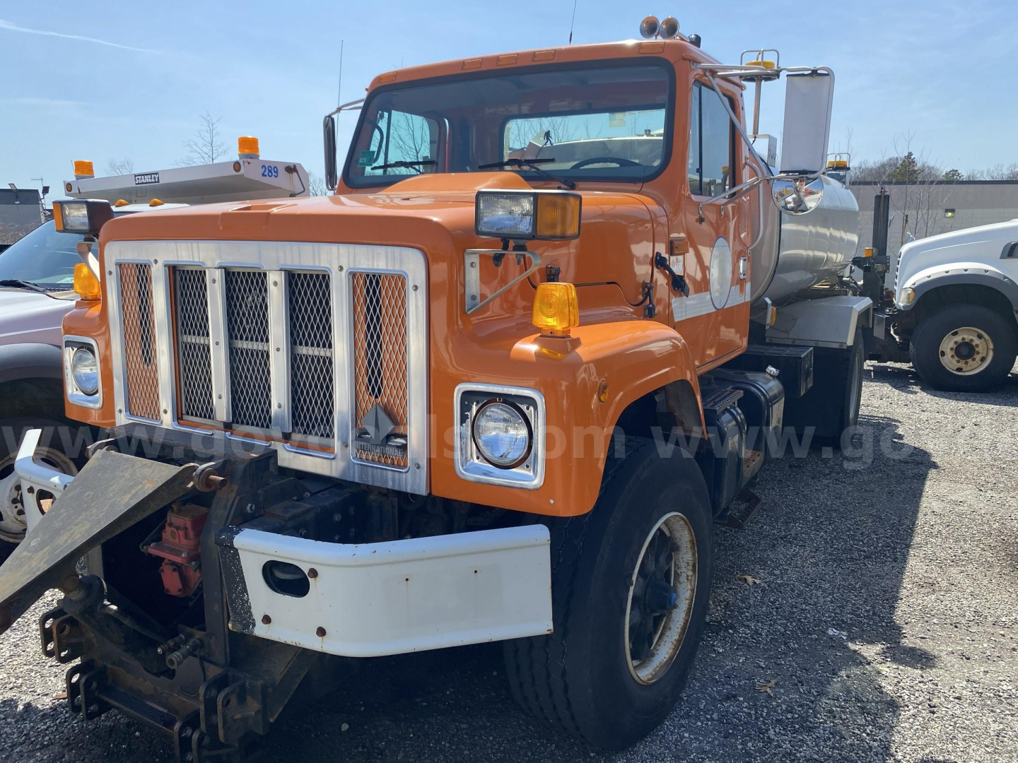 International 2574 truck with orange cab and attached water tanker in a lot.