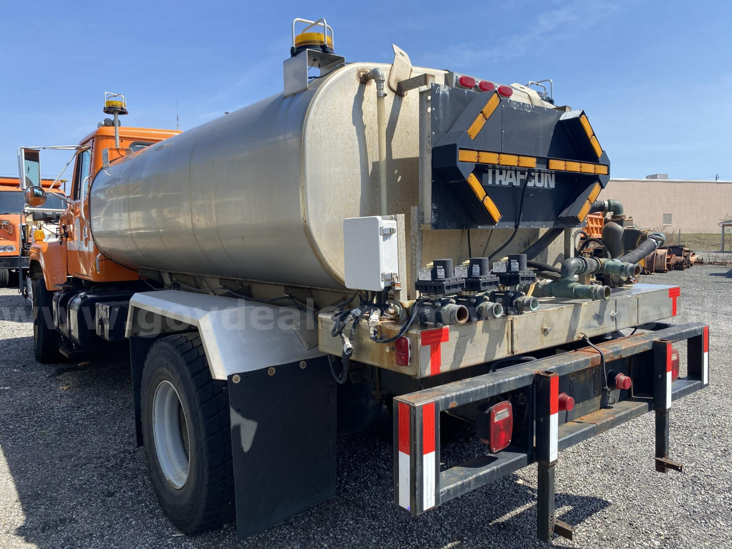 Rear view of a vacuum tanker truck mounted on a 2002 International 2574 chassis with a cylindrical stainless tank, rear hoses, and reflective safety markings.