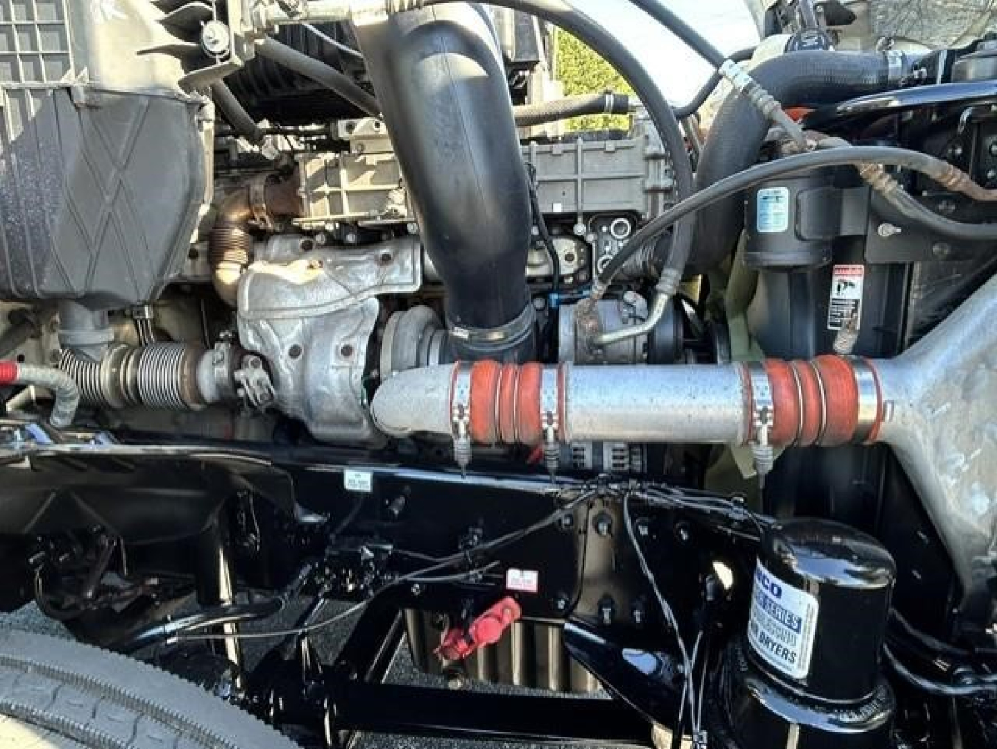 Freightliner Cascadia 126 engine bay showing intake pipe, hoses, and coolant reservoir with label, secondary filter, and wiring harness.