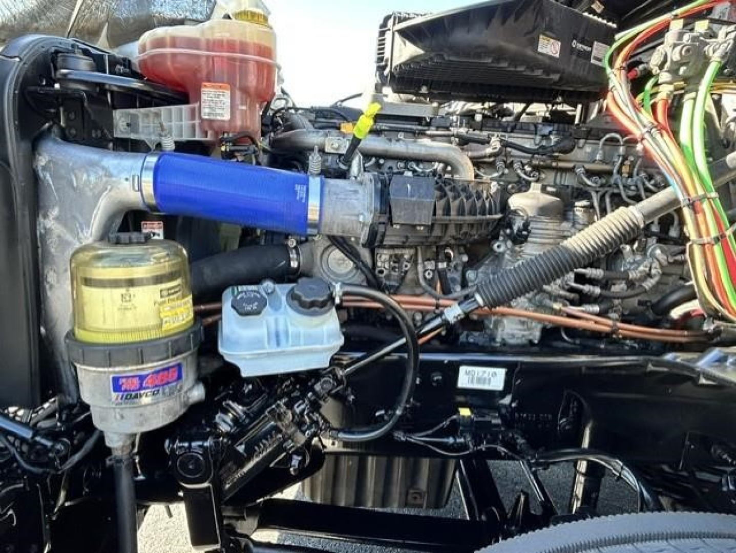 Engine bay of a 2021 Freightliner Cascadia 126 Day Cab showing blue intercooler pipe, coolant reservoir, oil filter, and labeled components.