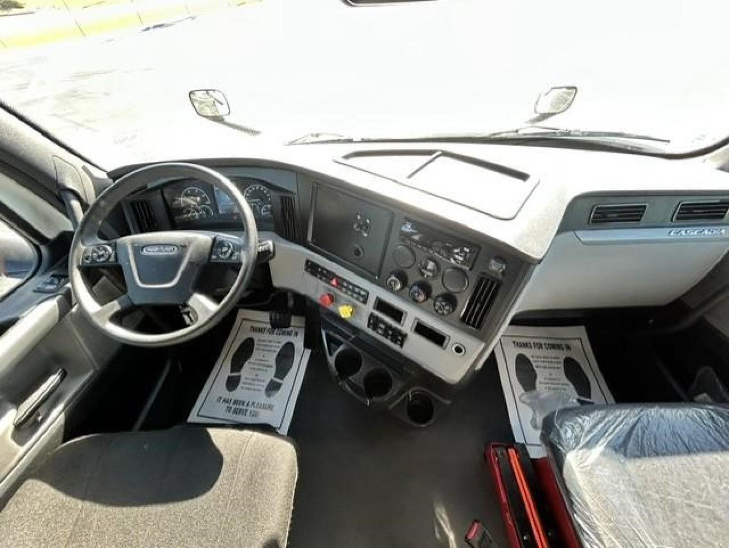 Cab interior of Freightliner Cascadia 126 day cab showing steering wheel, dashboard with gauges, center console, and front passenger seat.